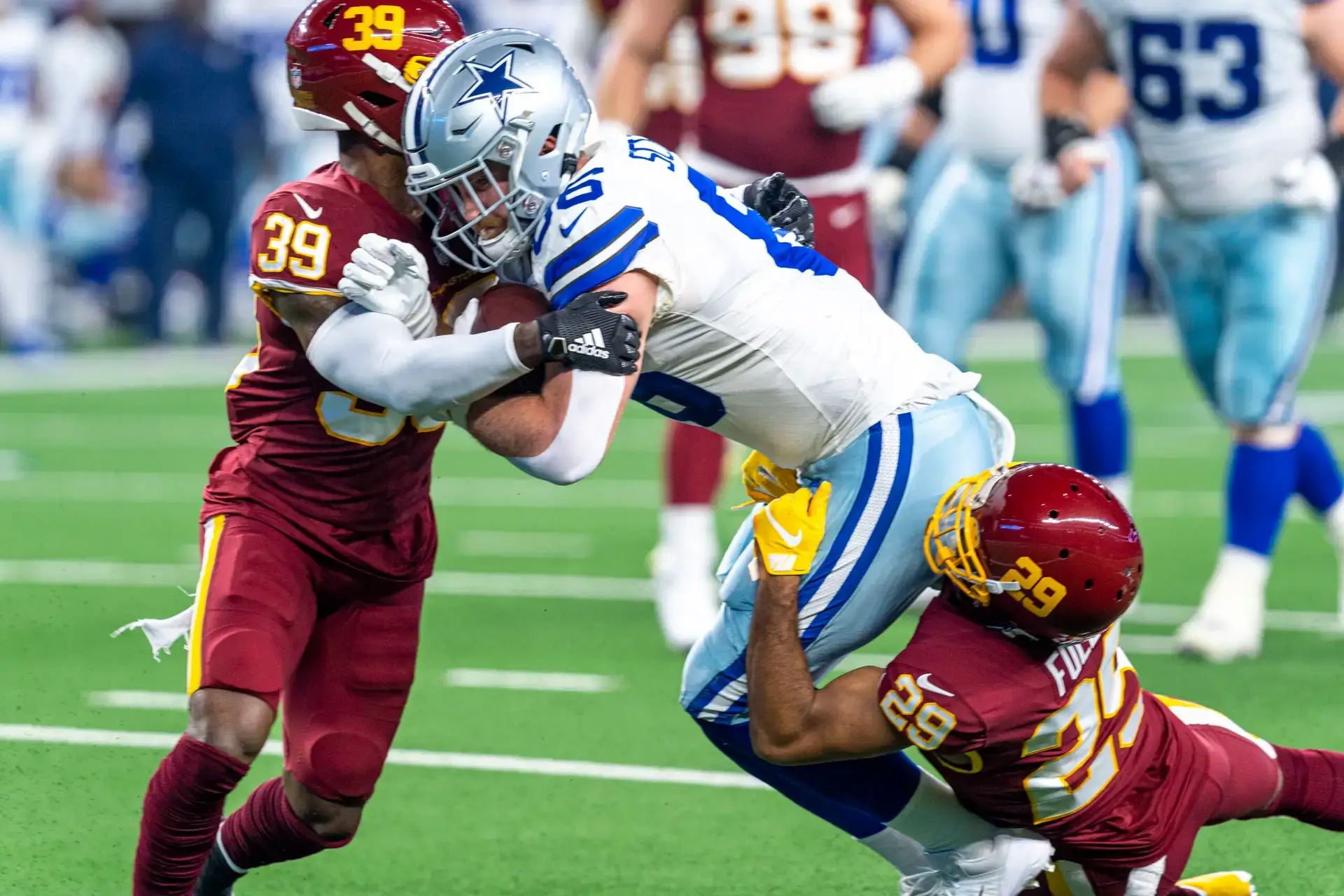 Dalton Schultz, entonces con los Dallas Cowboys, es tacleado por dos defensivos de Washington