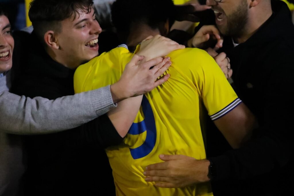 Futbolista celebrando un gol abrazado por la afición